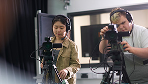 Two video production professionals operating television cameras in a studio.