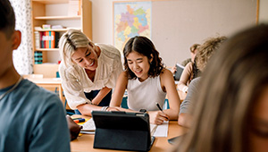 Teacher helping students work together on a classroom assignment using a tablet.