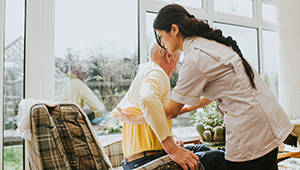Home healthcare worker smiling while assisting an older adult in a home setting.